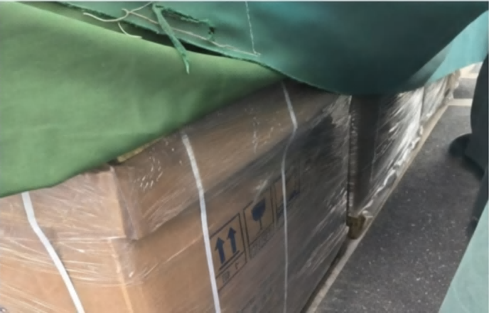 Operator holding an FYJ brand RFID handheld reader pointed toward a densely stacked and tarpaulin-covered storage bay, performing distant batch scanning for inventory count.